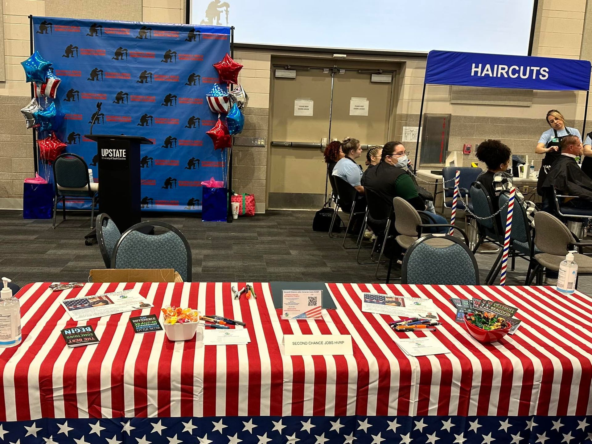 A table with a red white and blue striped tablecloth is in a room with people sitting at tables.