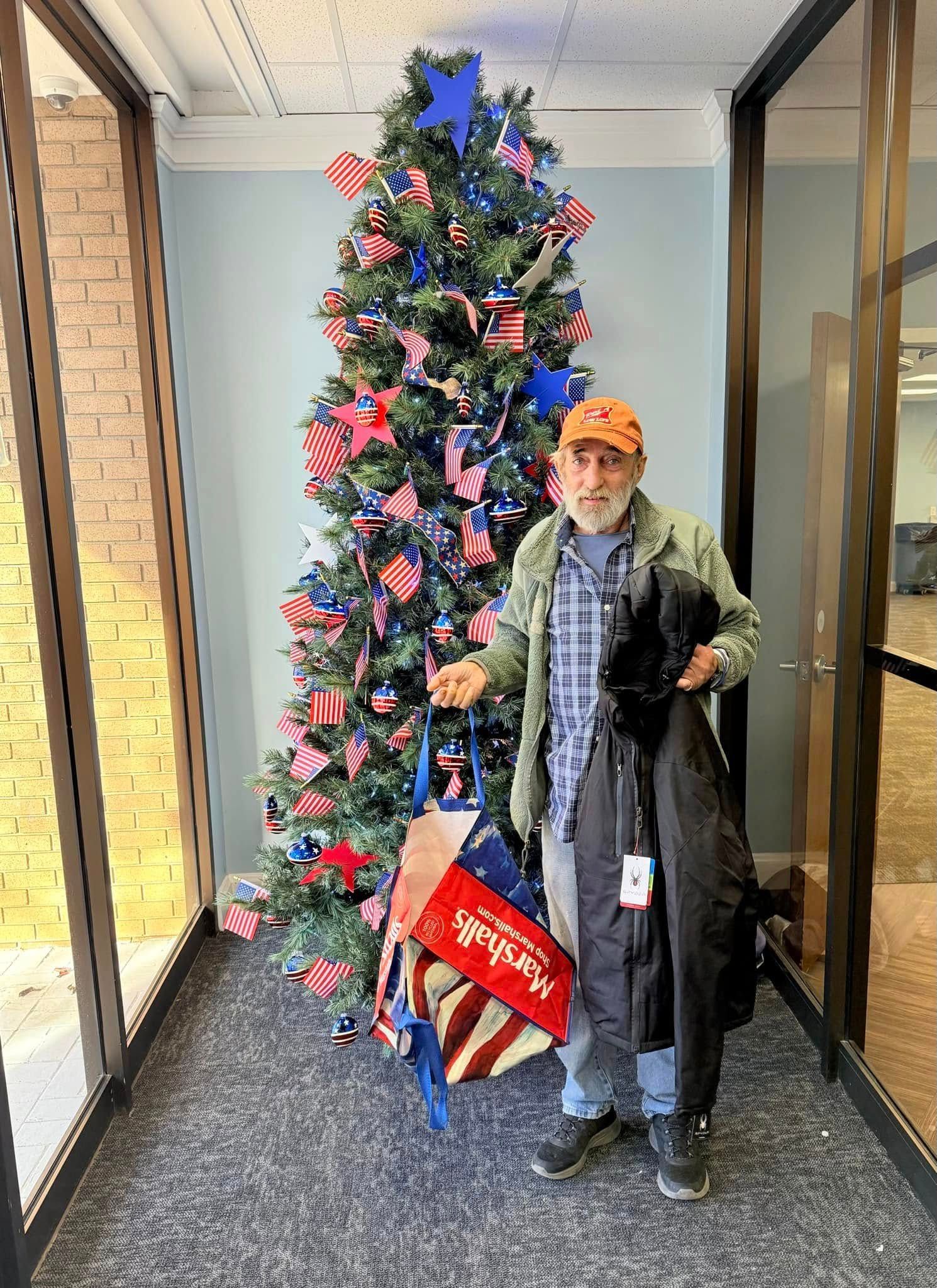 A man is standing in front of a christmas tree in a hallway.