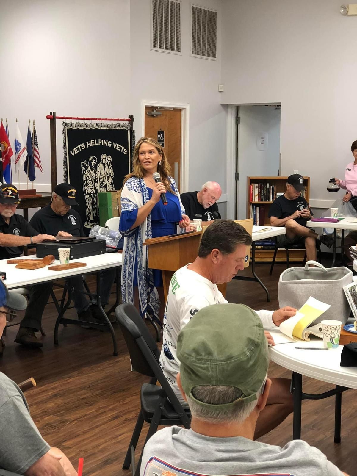 A woman is standing at a podium talking to a group of people sitting at tables.