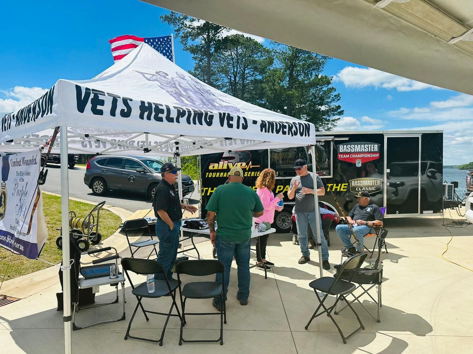 A group of people are standing under a tent that says ' vets helping vets ' on it.