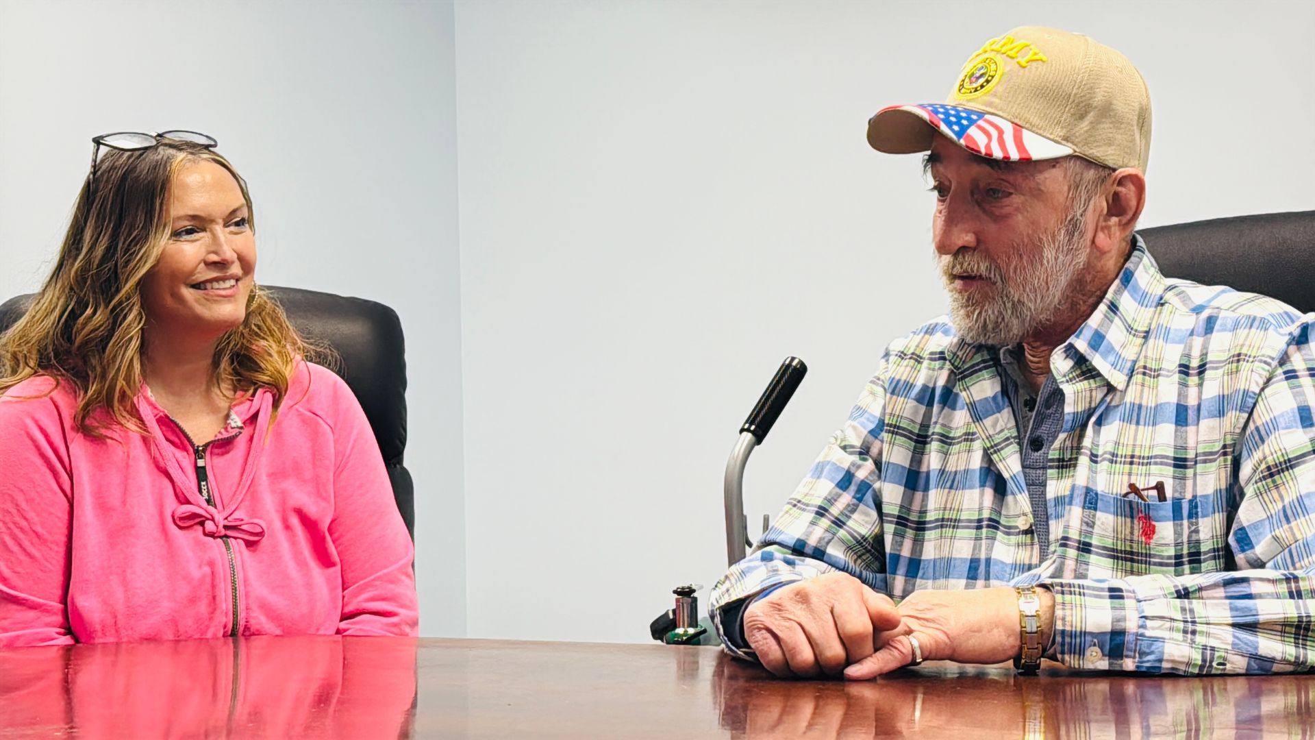 A man and a woman are sitting at a table in front of a microphone.