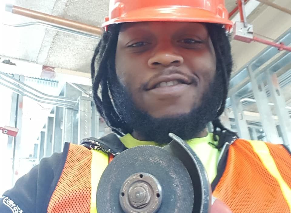 A man wearing a hard hat and safety vest is holding a grinding wheel