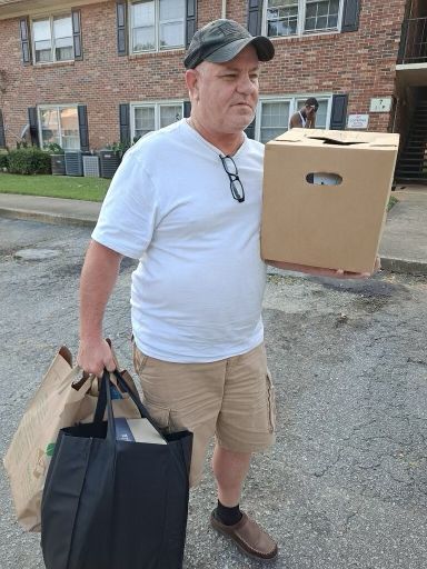 A man is holding a box and a bag in front of a brick building.