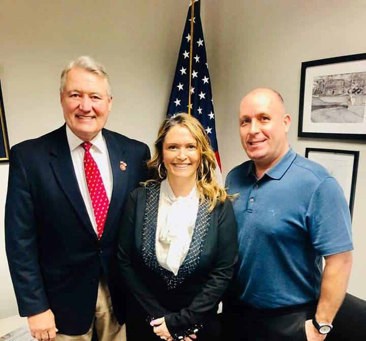 Three people posing for a picture in front of an american flag