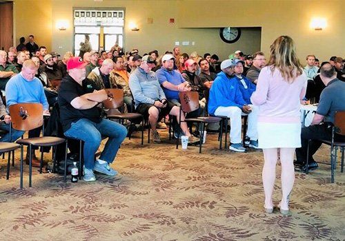 A woman is standing in front of a large group of people sitting in chairs