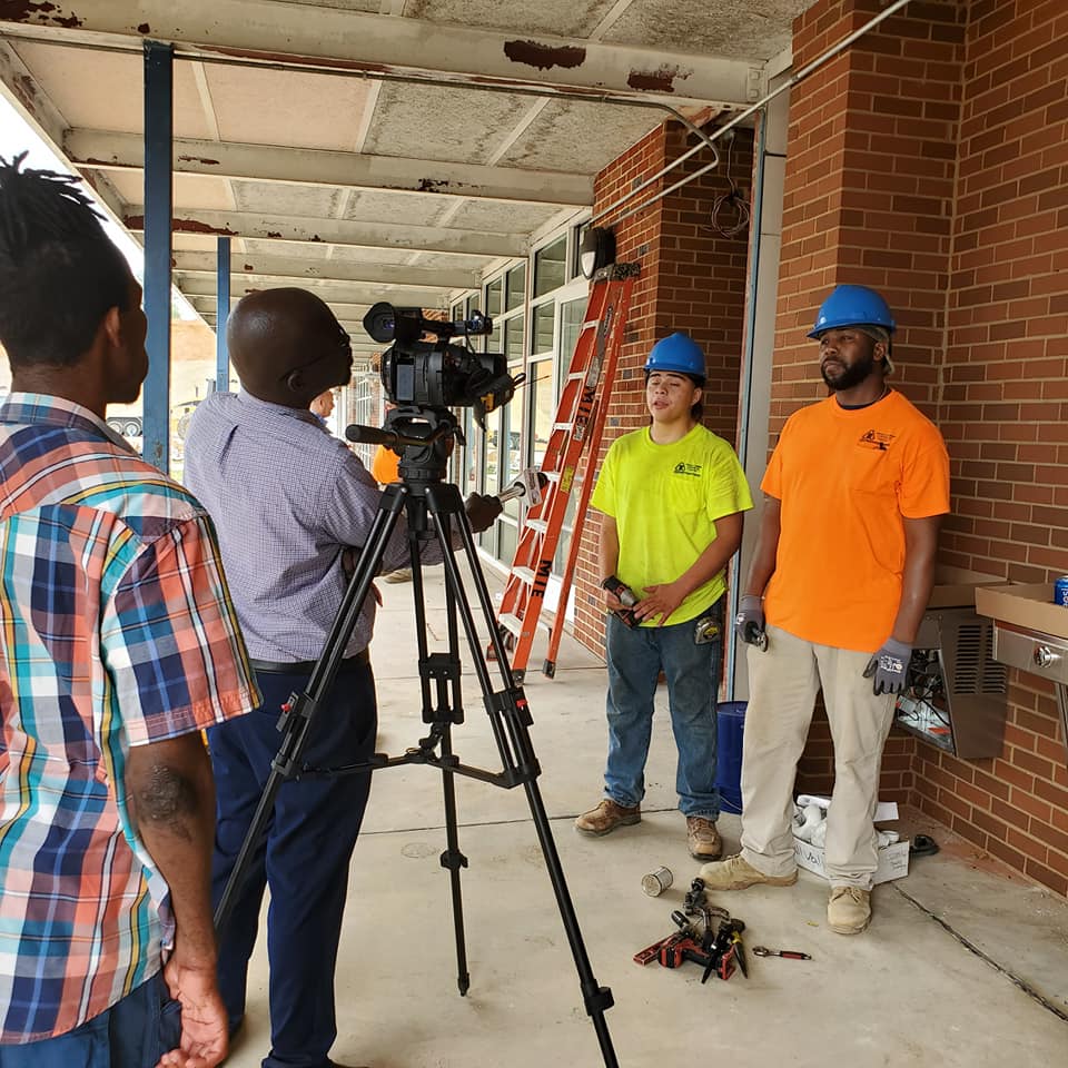 A group of construction workers are standing in front of a camera on a tripod