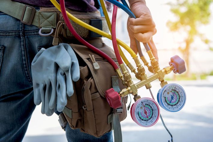 HVAC technician holding manifold gauges and tools from a work belt.