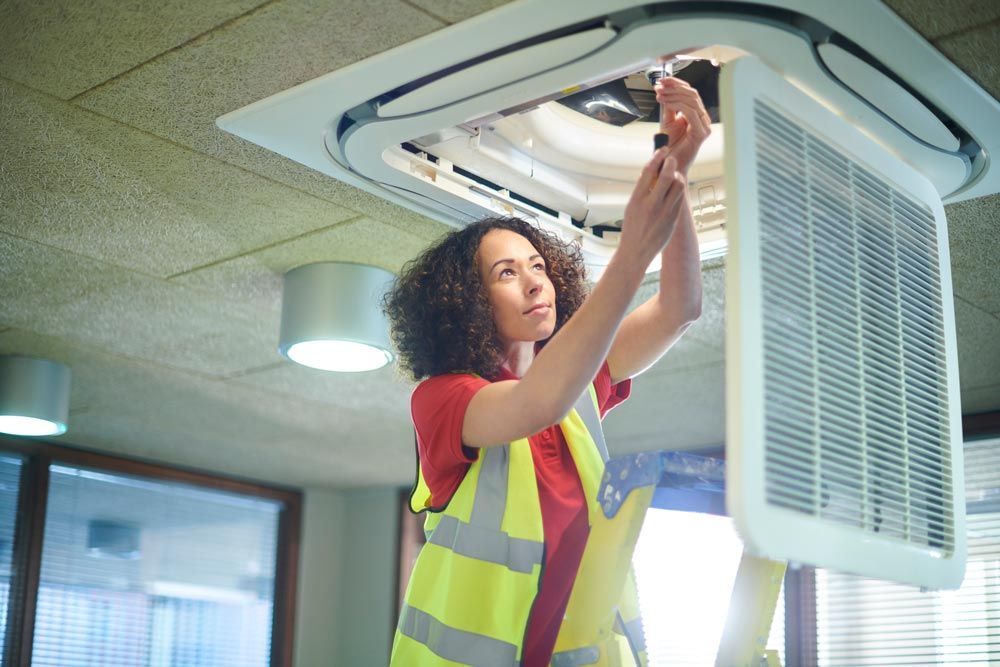 A woman in a safety vest fixes an air conditioner, emphasizing commercial HVAC service providers in