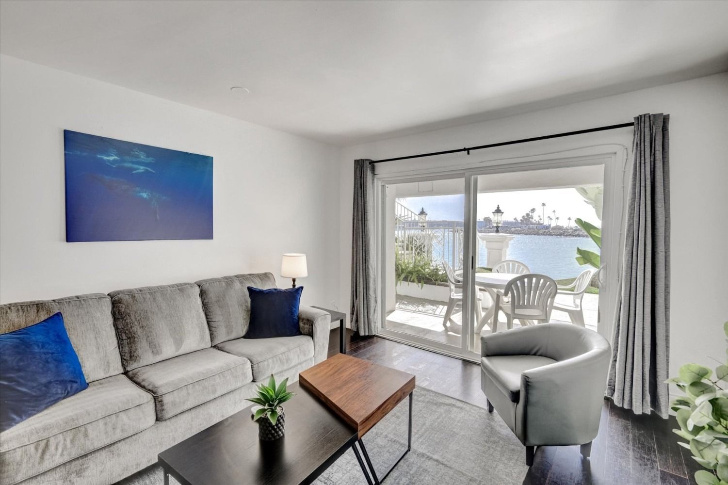 A cozy living room with a gray sofa, a small coffee table, and an armchair, facing a sliding door overlooking the water.