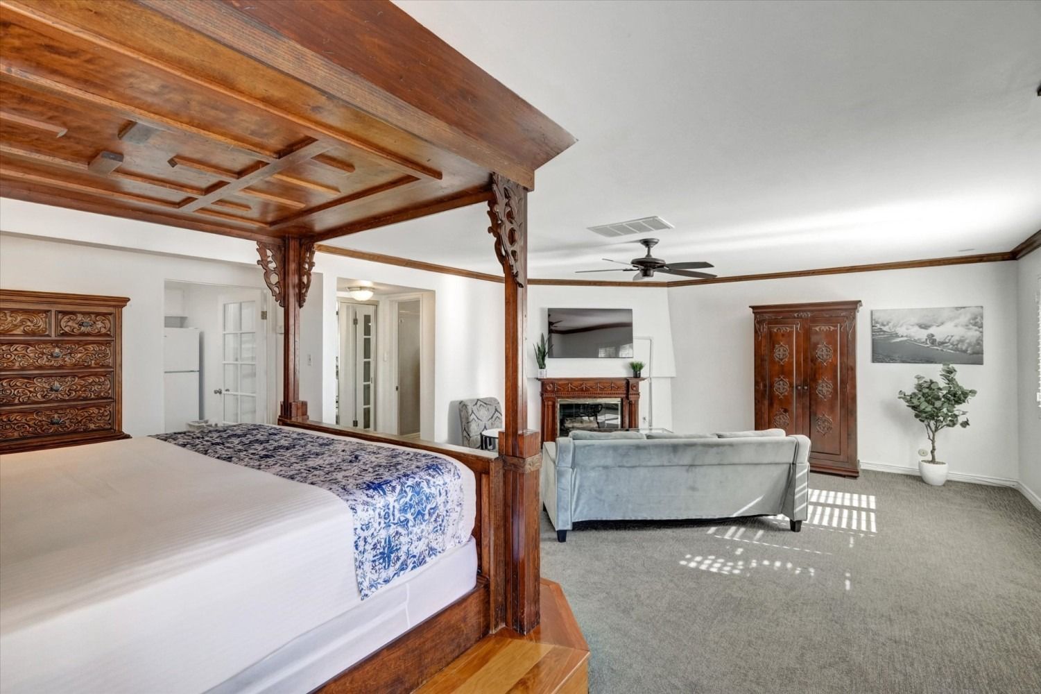 A spacious bedroom featuring a large wooden four-poster bed, a light blue sofa in front of a fireplace, and an armoire.