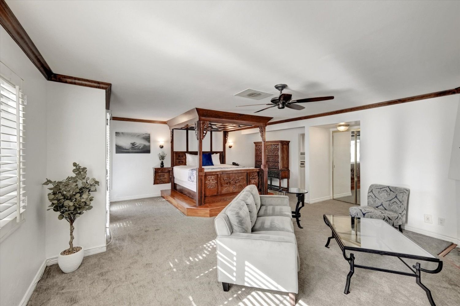 A spacious bedroom featuring a large canopy bed on a raised wooden platform, a sofa, armchair, and coffee table.