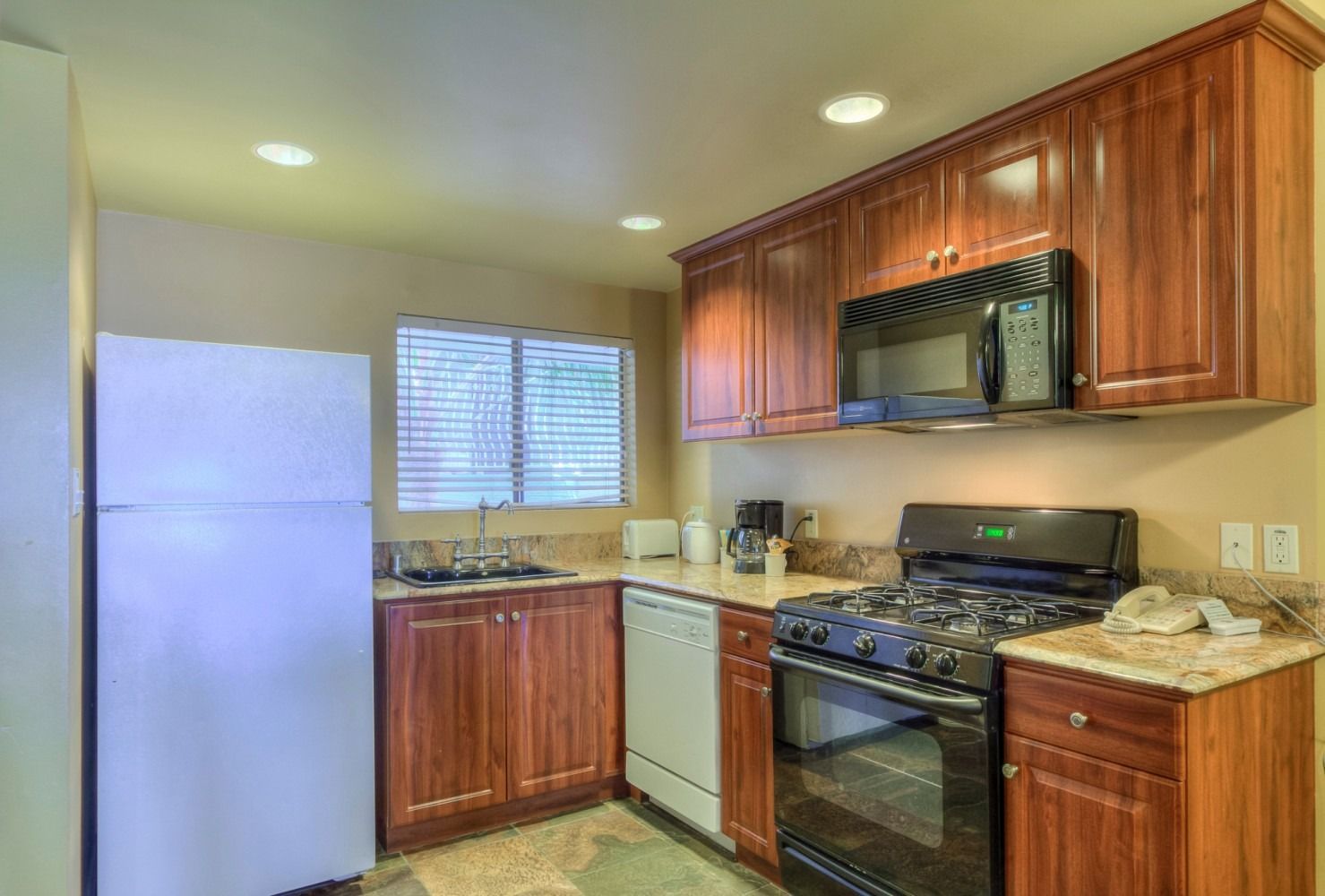 A kitchen with wood cabinets, a white refrigerator, a black oven and microwave, and a window above the sink.