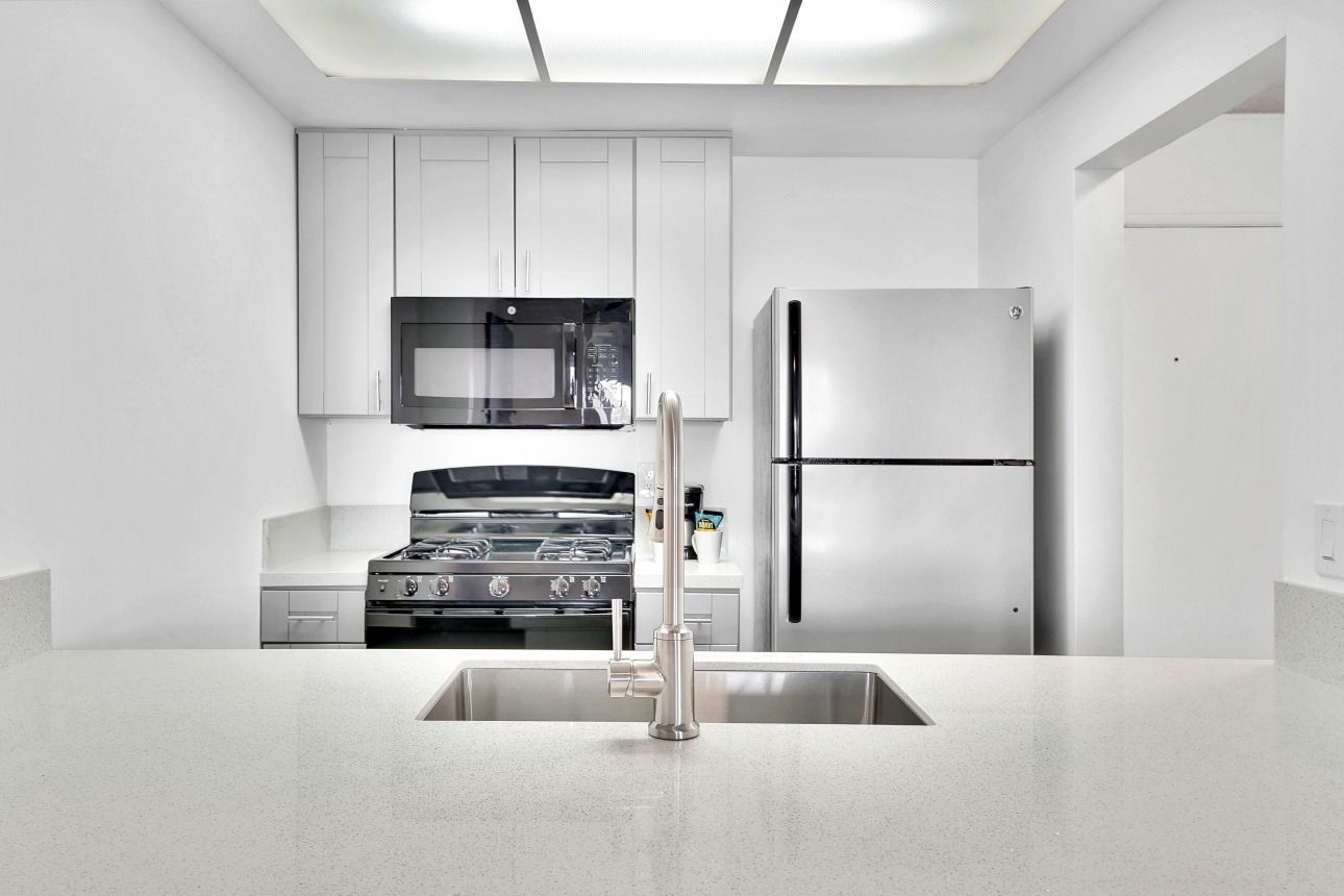 A modern kitchen with white cabinets, stainless steel appliances, and a quartz countertop island with a sink.