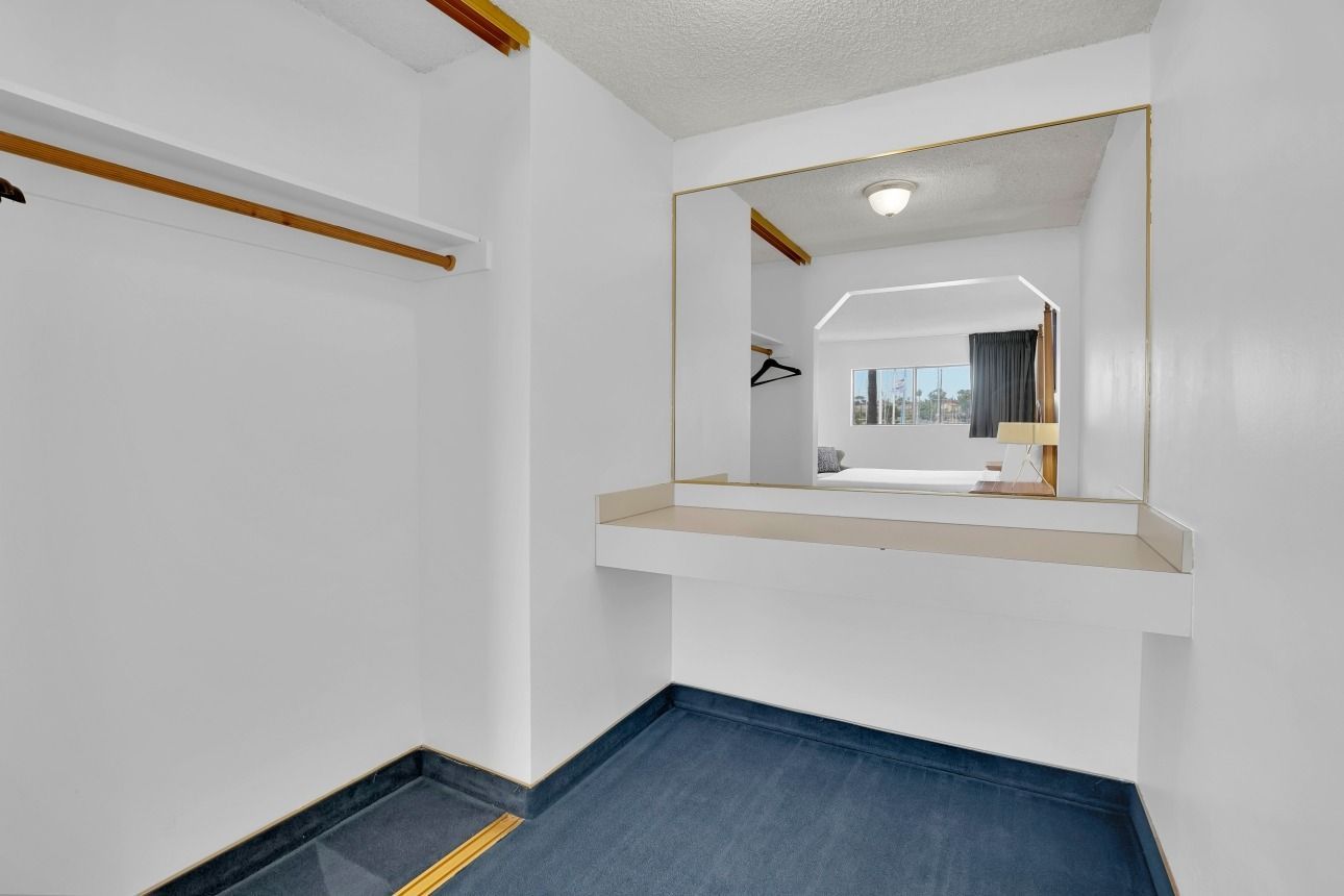 A small, white dressing area with a wall-mounted vanity, large mirror, closet rack, and blue carpet.