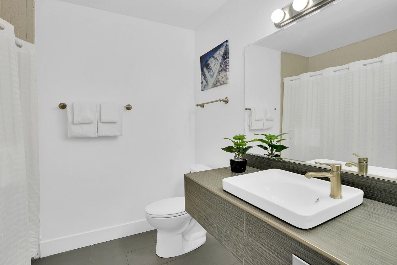 Modern bathroom featuring a white vanity with a gold faucet, a toilet, and a white shower curtain against white walls.