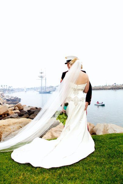 Bride and military groom at waterside wedding. Bride's dress train and veil flowing.