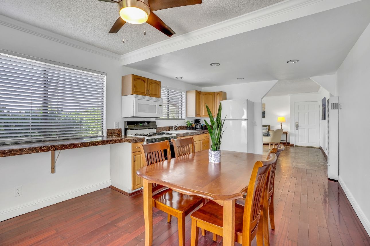 Dining room with wooden table, chairs, kitchen, and hardwood floors.