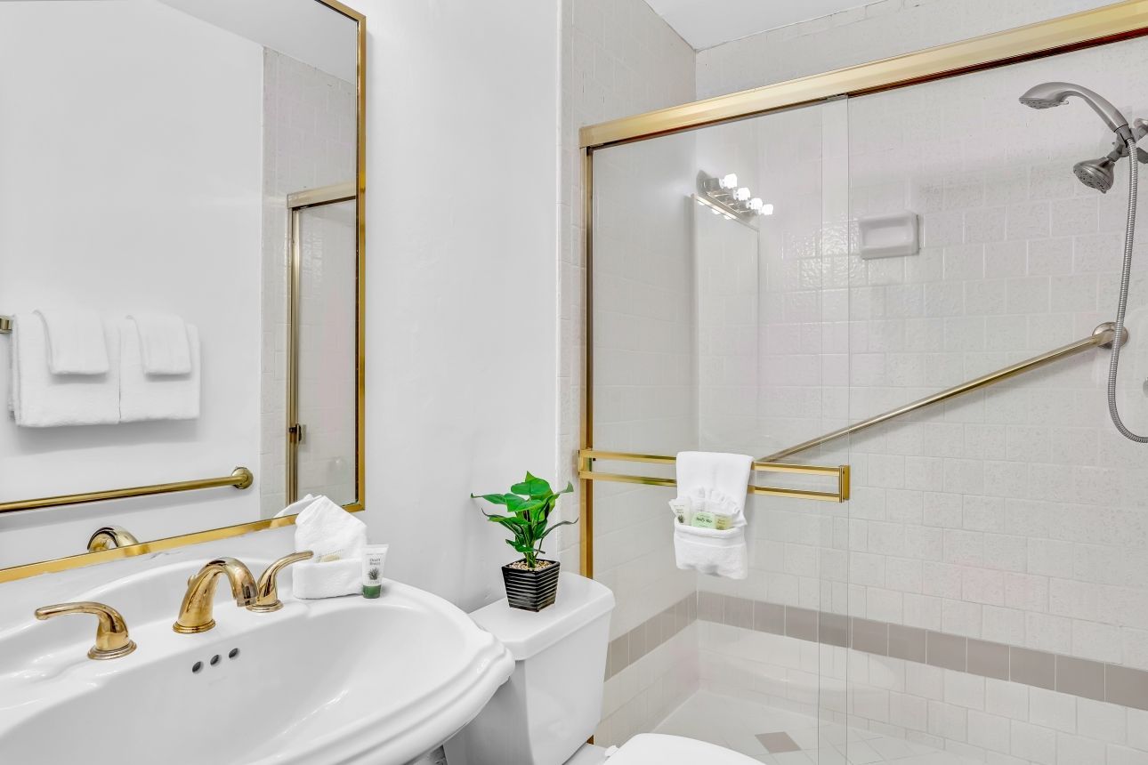 Bathroom with white walls, gold fixtures, a glass shower, and a sink with a white towel.