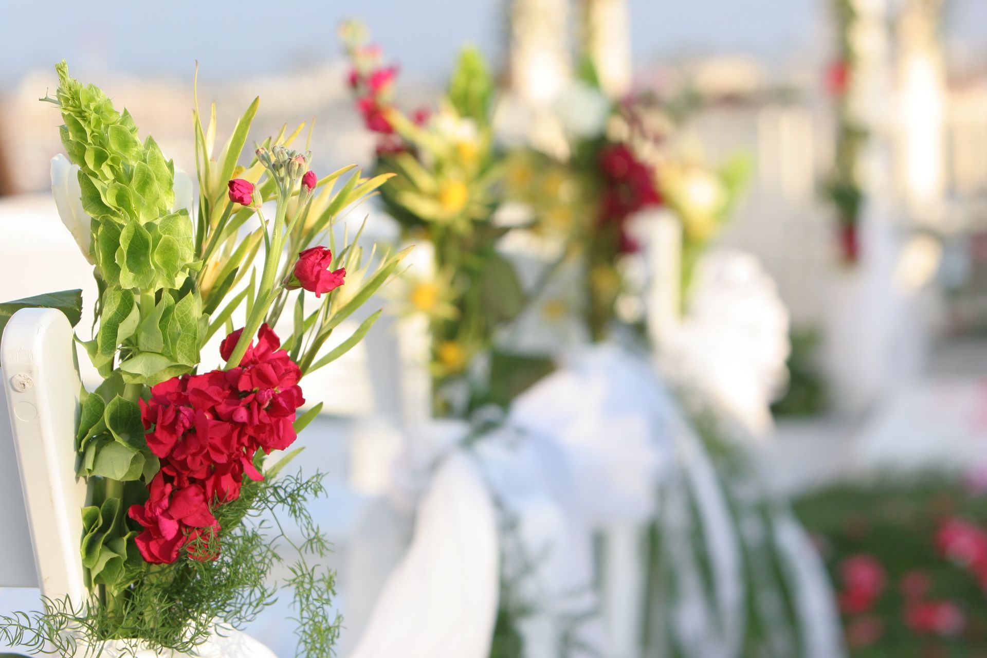Red and green flowers decorate white chairs at an outdoor event.