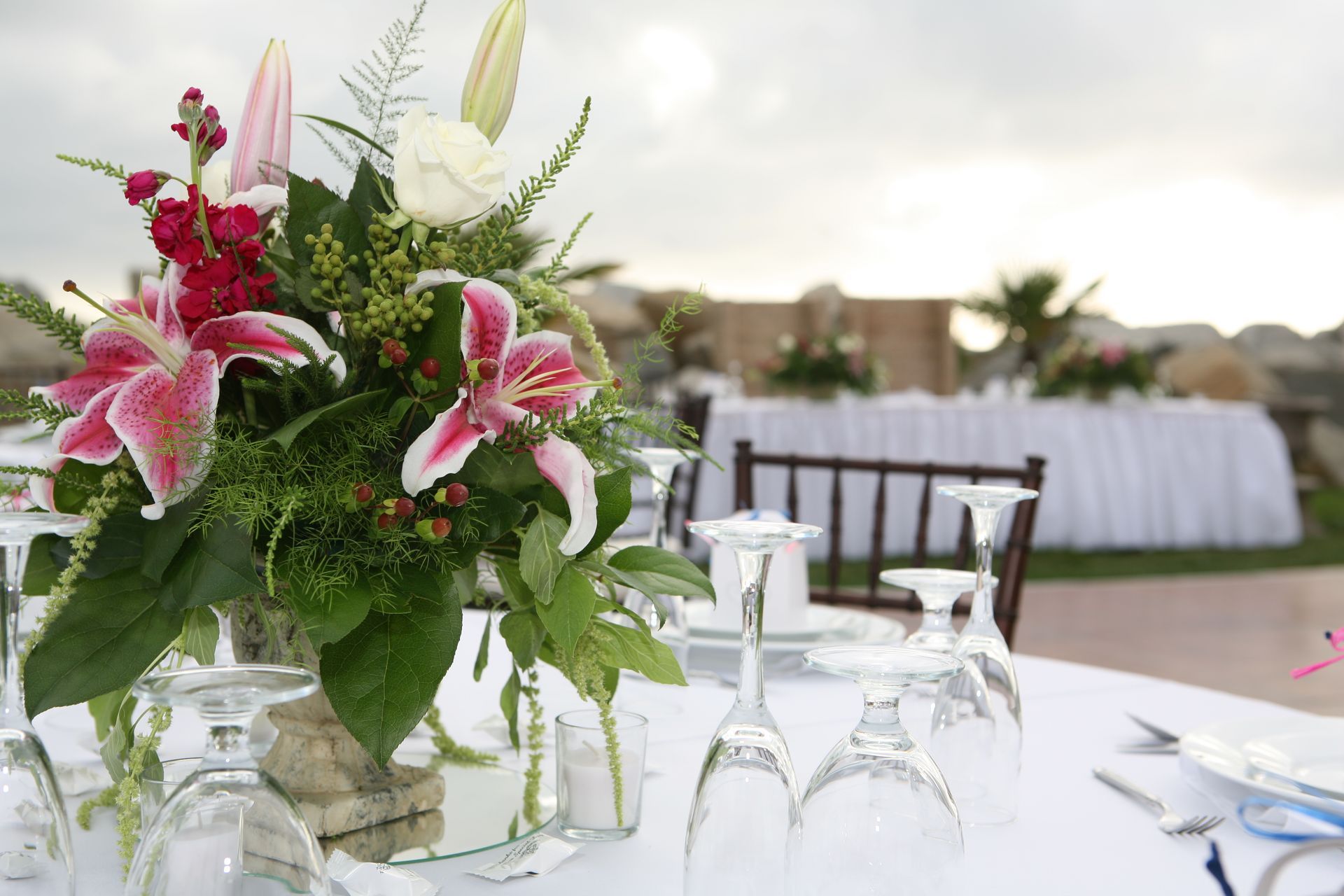 Floral centerpiece on a wedding table with place settings; other tables in background.