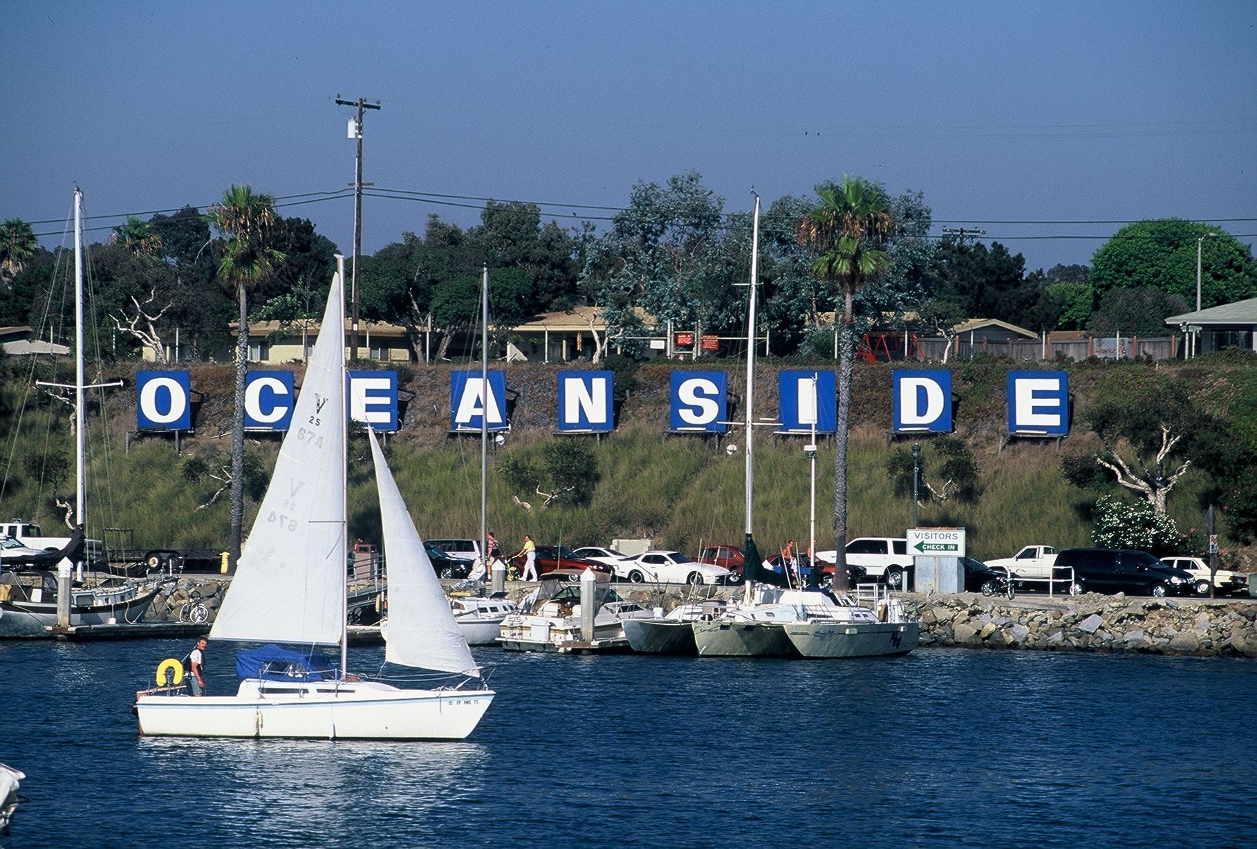 Sailboat in Oceanside harbor with the city's sign in the background.
