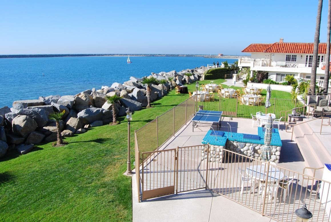 Lush green lawn, blue water, and white buildings by the coast on a sunny day.