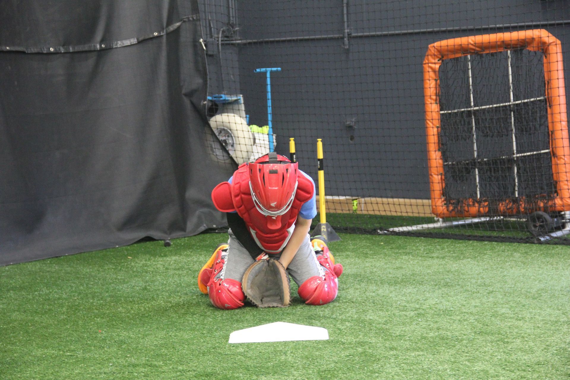 A baseball catcher is kneeling on the grass holding a glove.