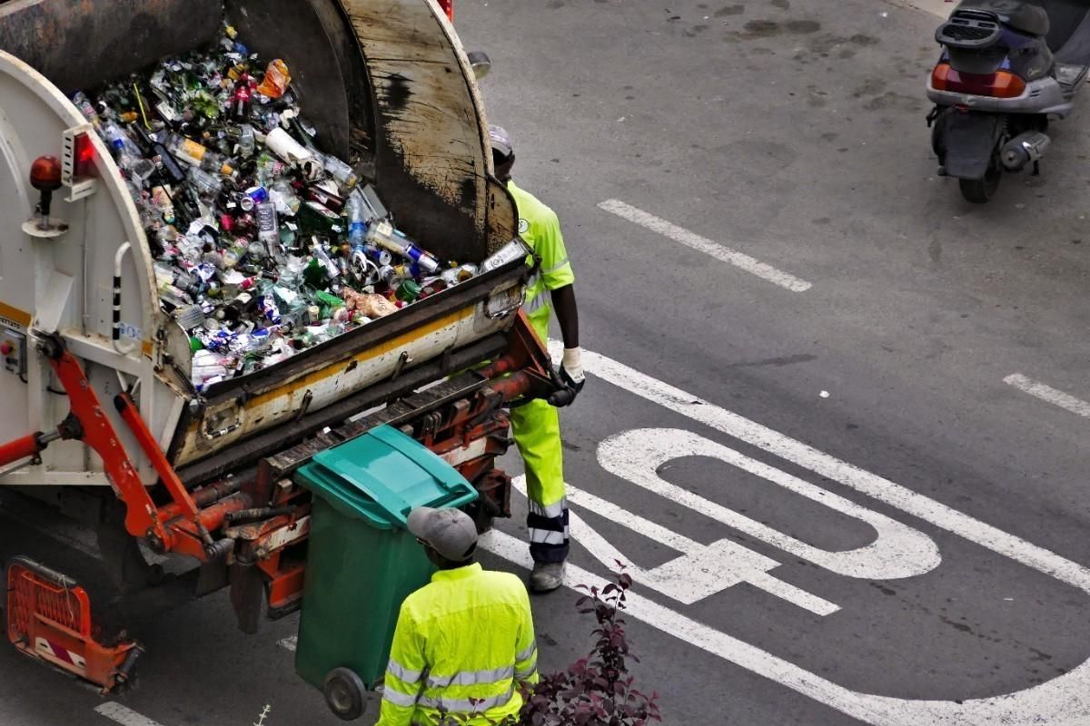 a garbage truck is full of garbage and two men are standing next to it .