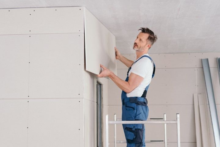 Man in blue overalls installing a white cabinet in a room under construction