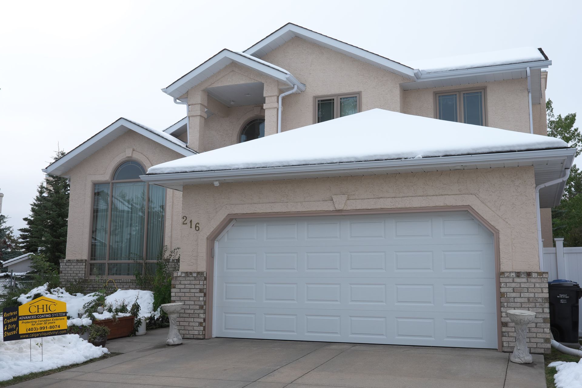 A large house with a white garage door and snow on the roof