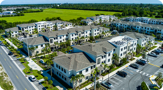 Aerial view of a modern apartment complex with parking lots and green fields surrounding it.