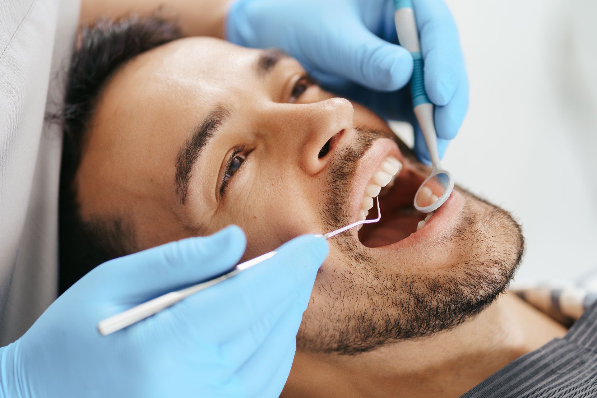 Hombre con la boca abierta en la consulta del dentista, recibiendo una revisión dental. Manos enguantadas del dentista con instrumentos.