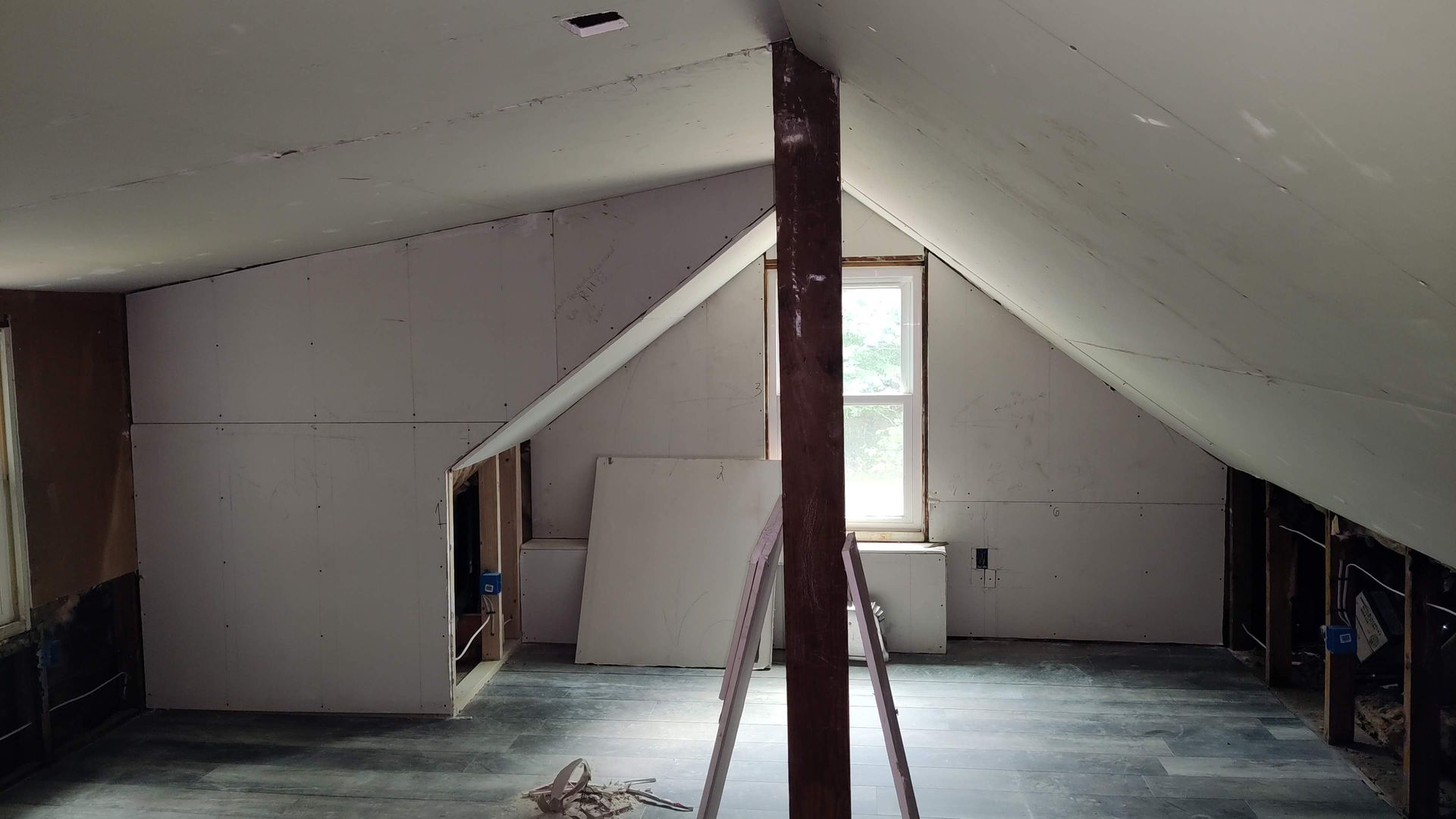 An empty attic with a ladder and a window.