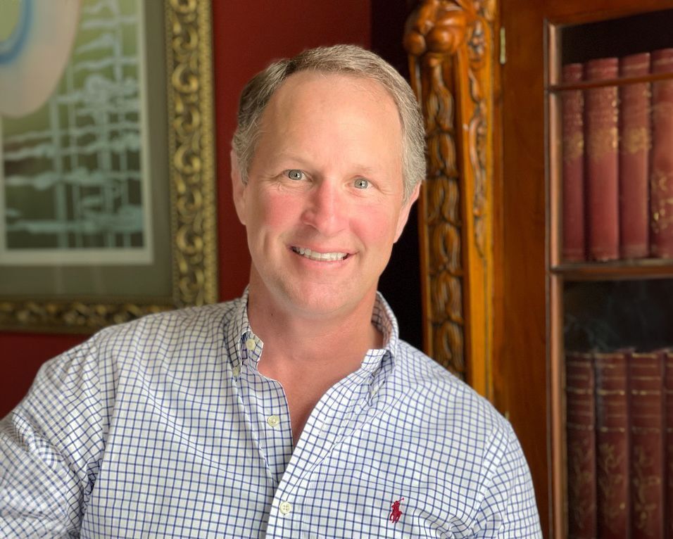 A man in a plaid shirt is smiling in front of a bookshelf.