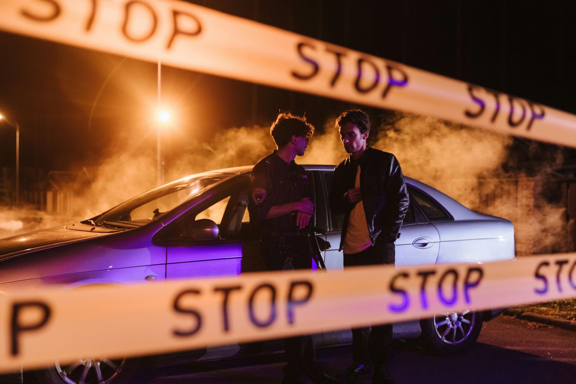Two men are standing next to a car behind a stop tape.