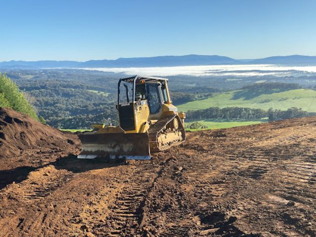 A bulldozer is driving down a dirt road with mountains in the background.