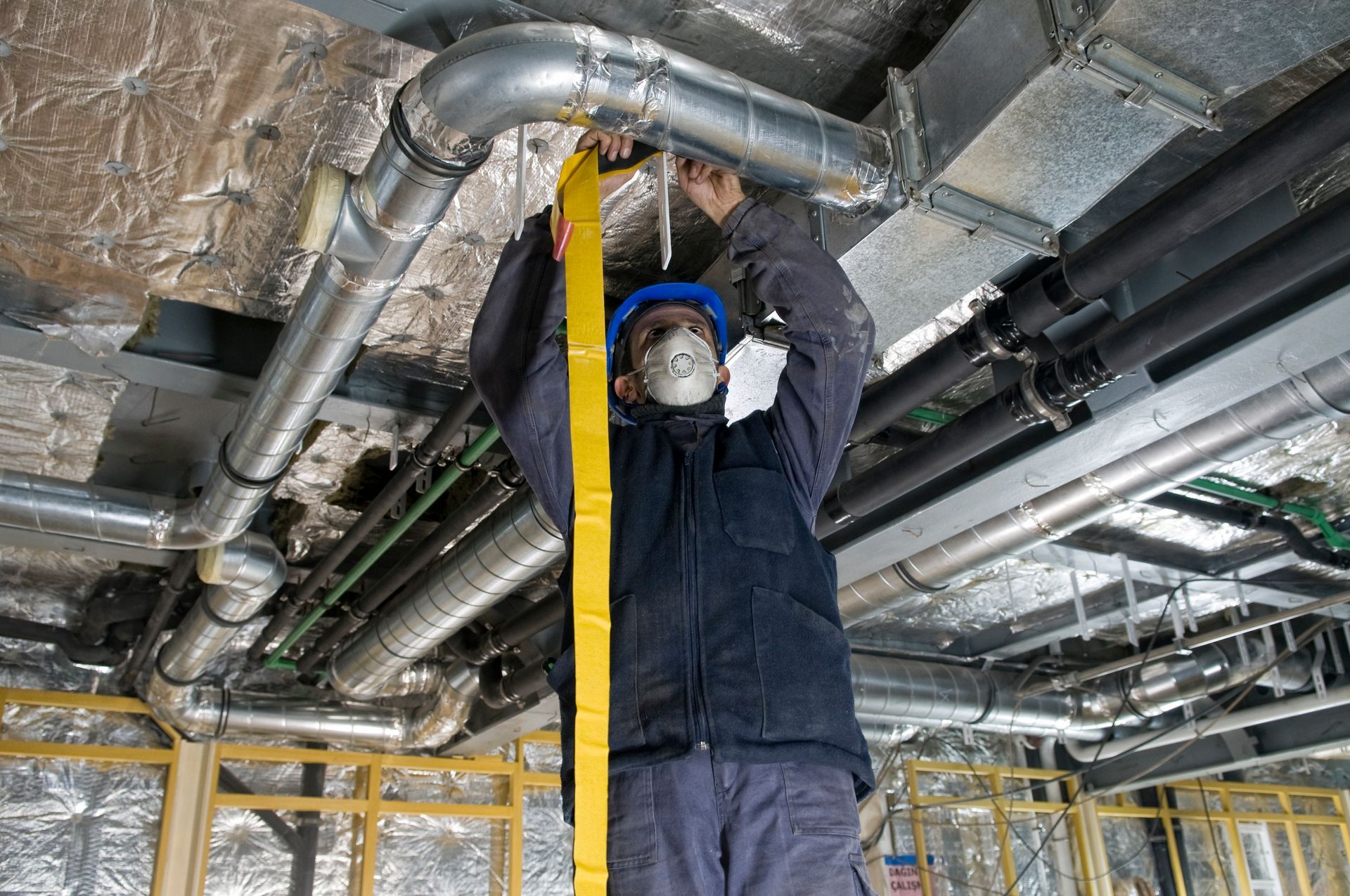 Worker wrapping an HVAC air duct with foil tape.