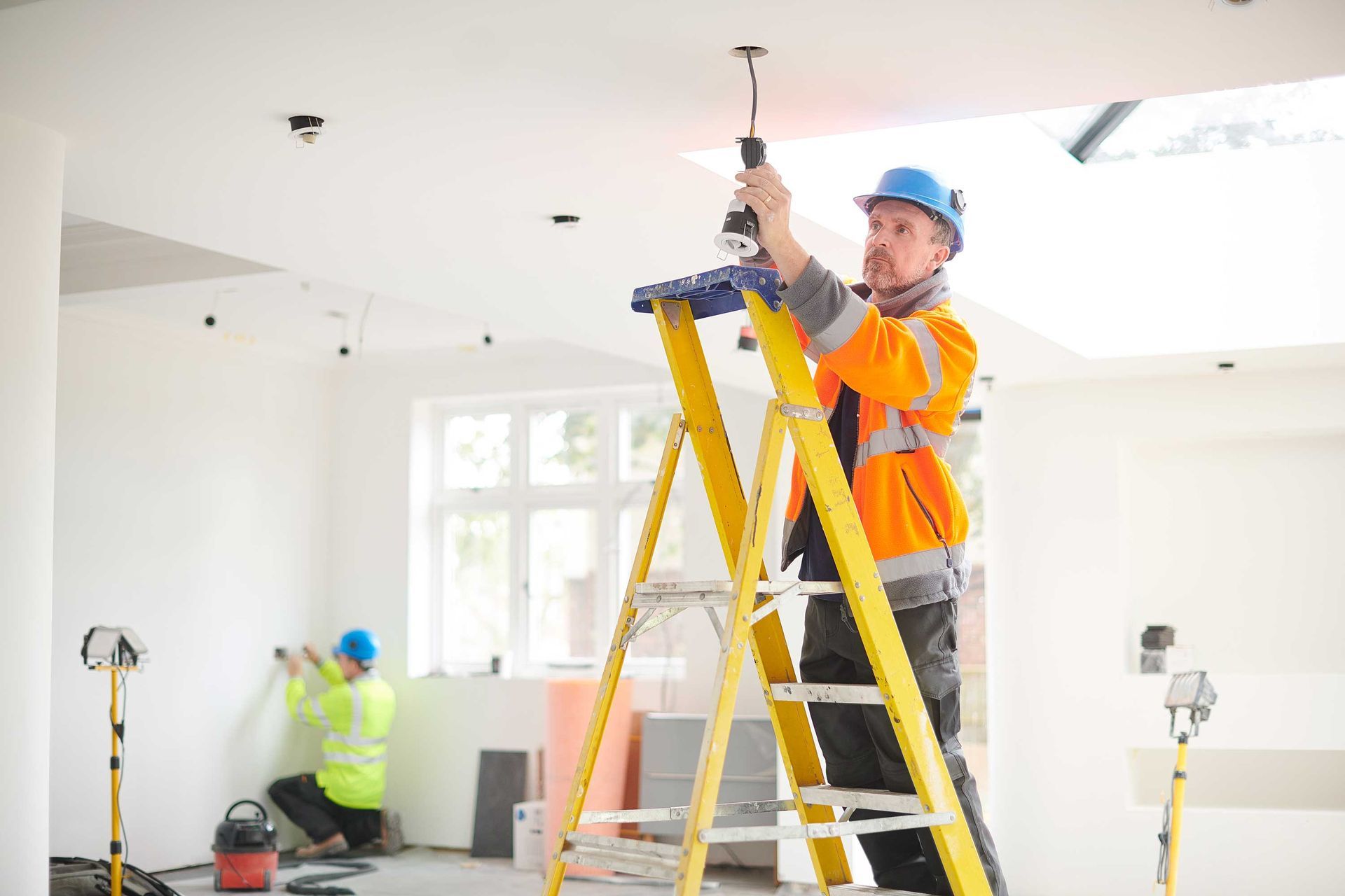 A man is standing on a ladder working on a light fixture.