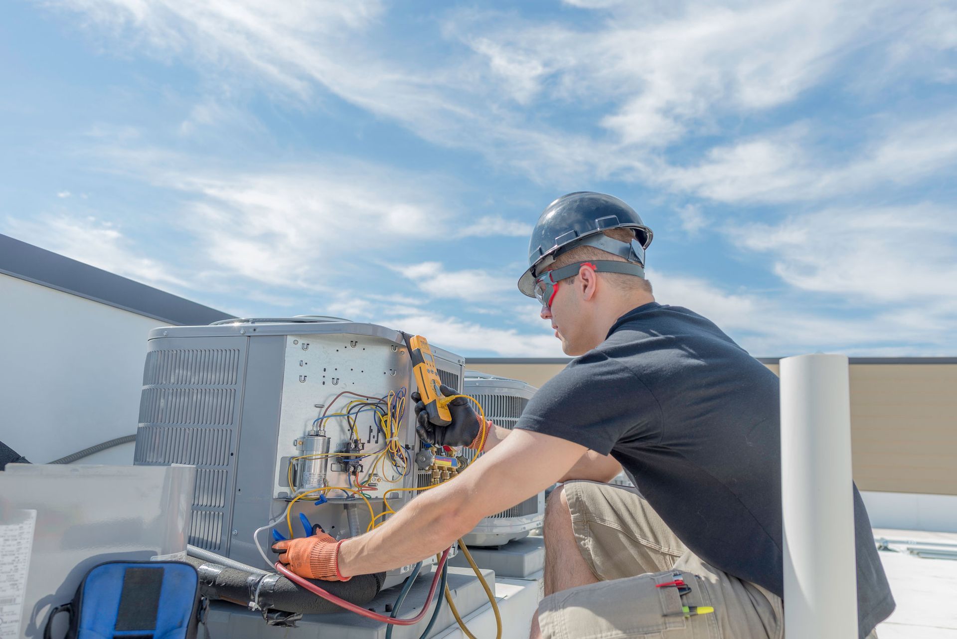 A man is working on an air conditioner on the roof of a building.