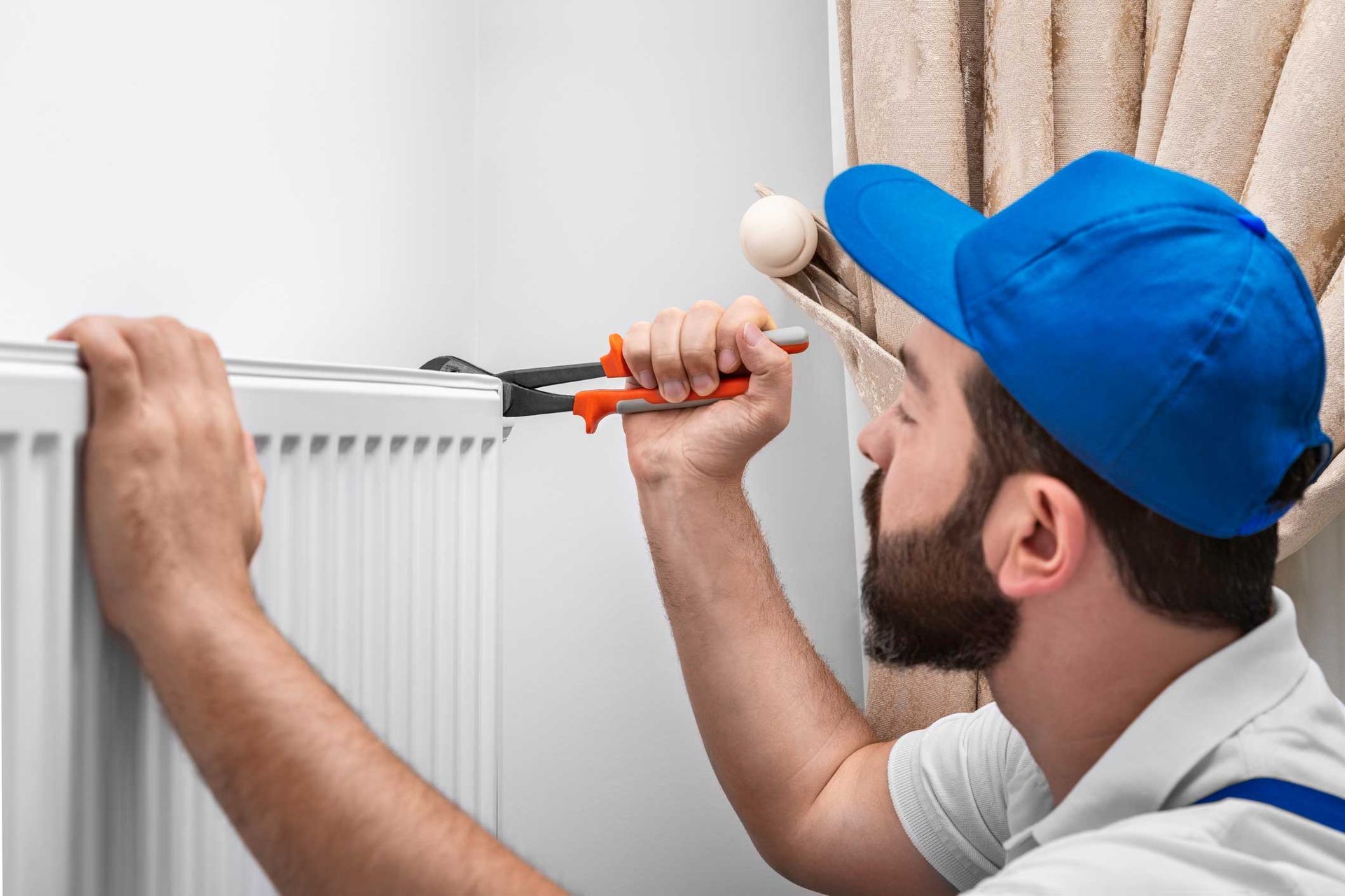 A man is fixing a radiator with a pair of pliers.