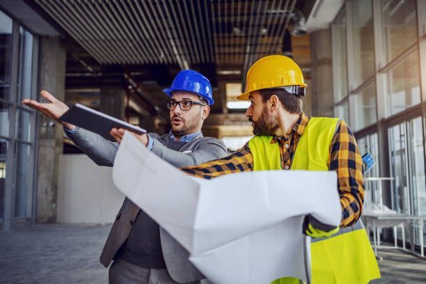 Two construction workers are looking at a blueprint in a building under construction.