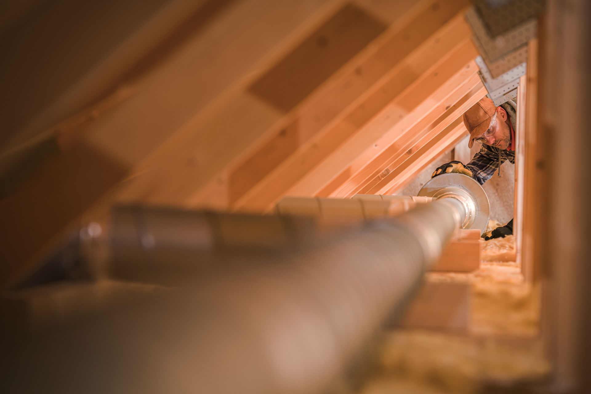 A man is working on a pipe in an attic.