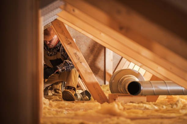A man is working on a pipe in an attic.