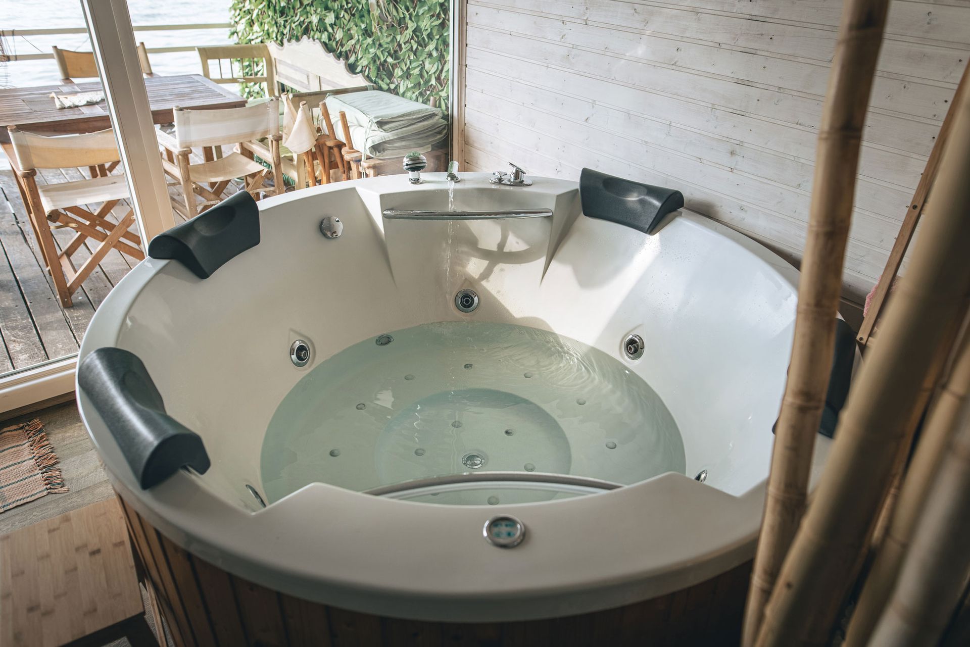 A round jacuzzi tub filled with water in a bathroom next to a window.
