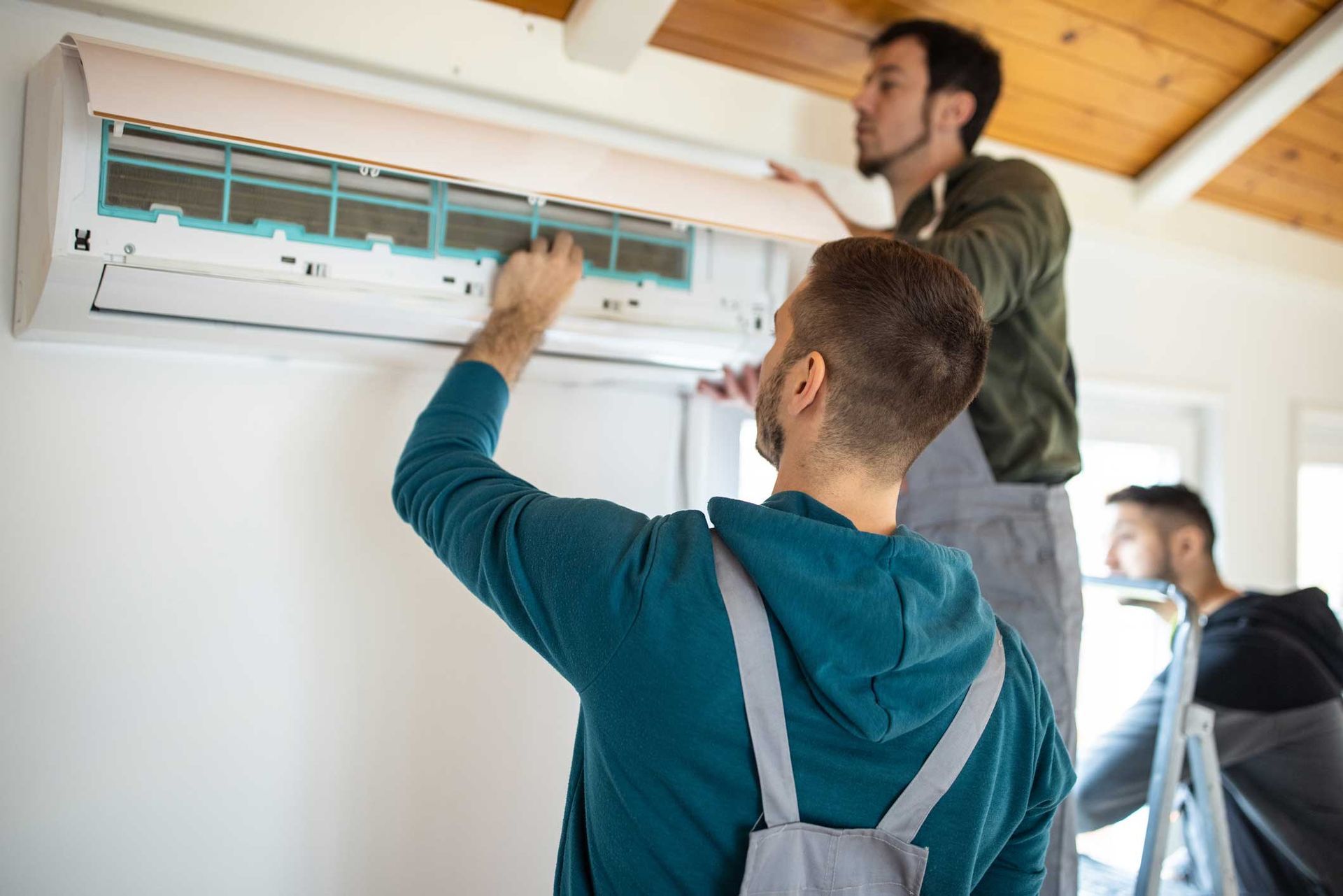 Two men are working on an air conditioner in a room.