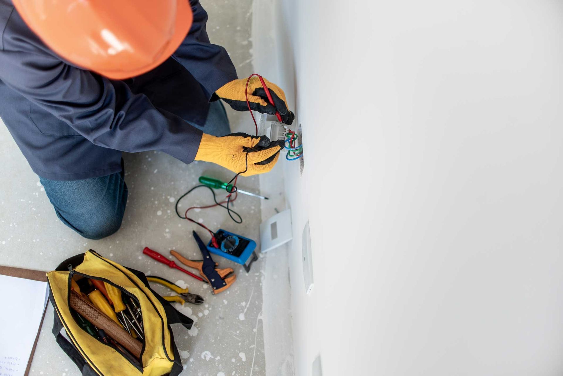 An electrician is working on an electrical outlet on a wall.