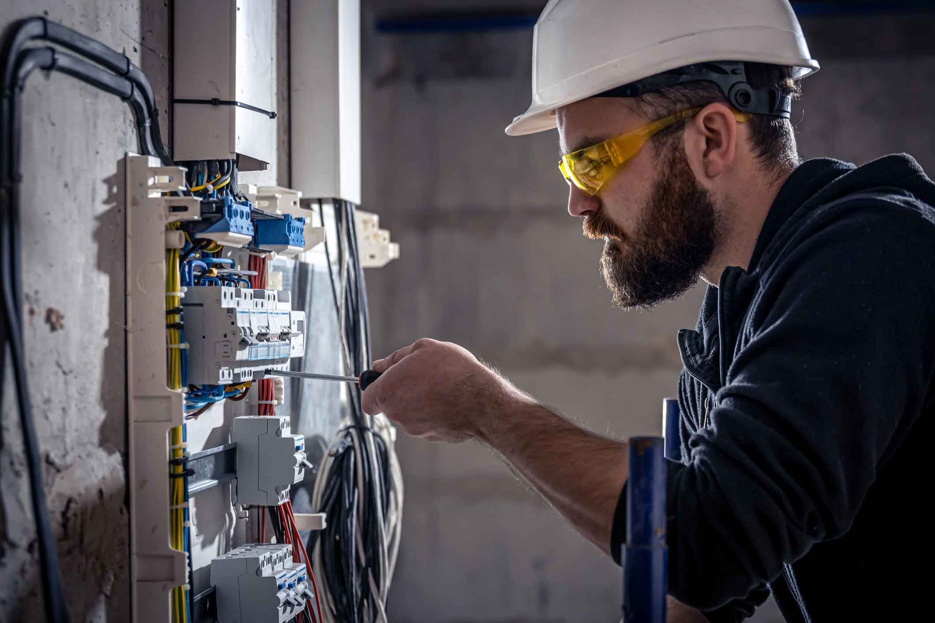 A man wearing a hard hat and goggles is working on an electrical box.