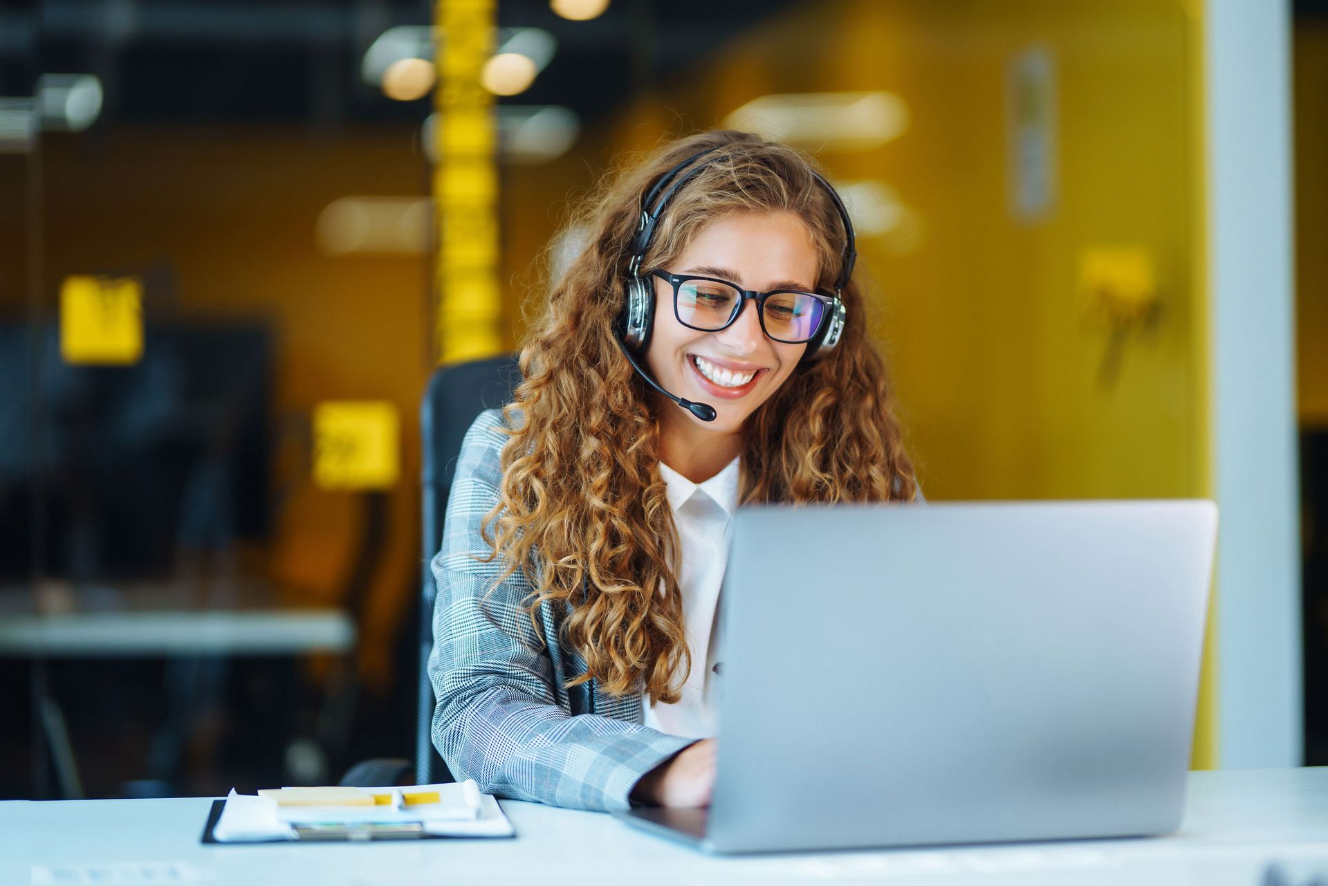 A woman wearing headphones and glasses is sitting in front of a laptop computer.