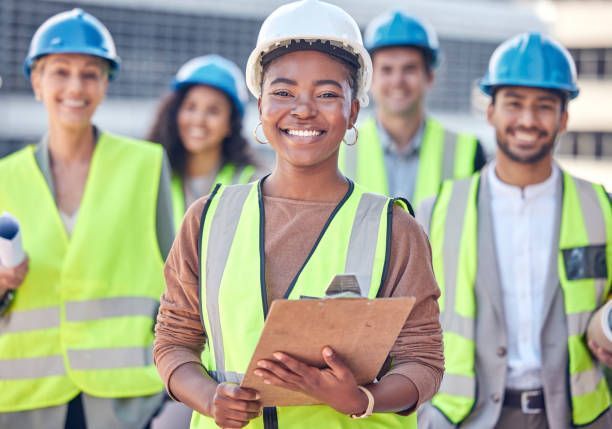 A woman is holding a clipboard in front of a group of construction workers.
