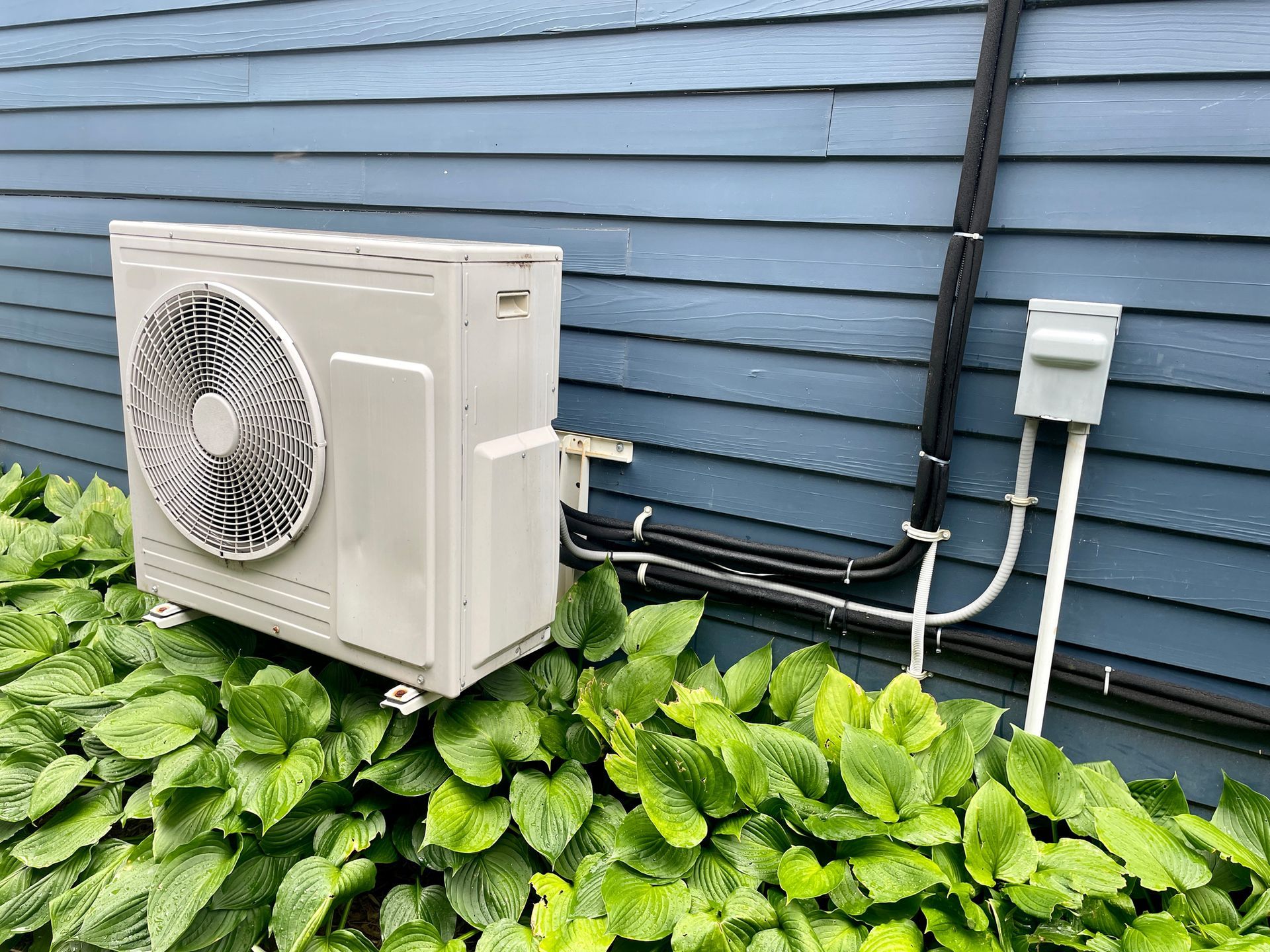 A white air conditioner is sitting on the side of a blue house.